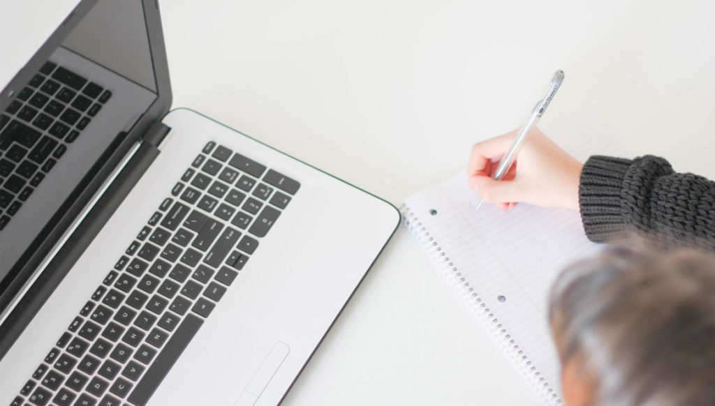 person writing and working at laptop