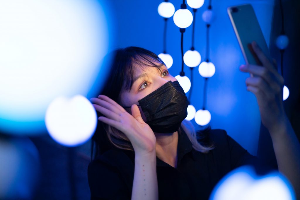 woman in a black mask waving at her phone's camera