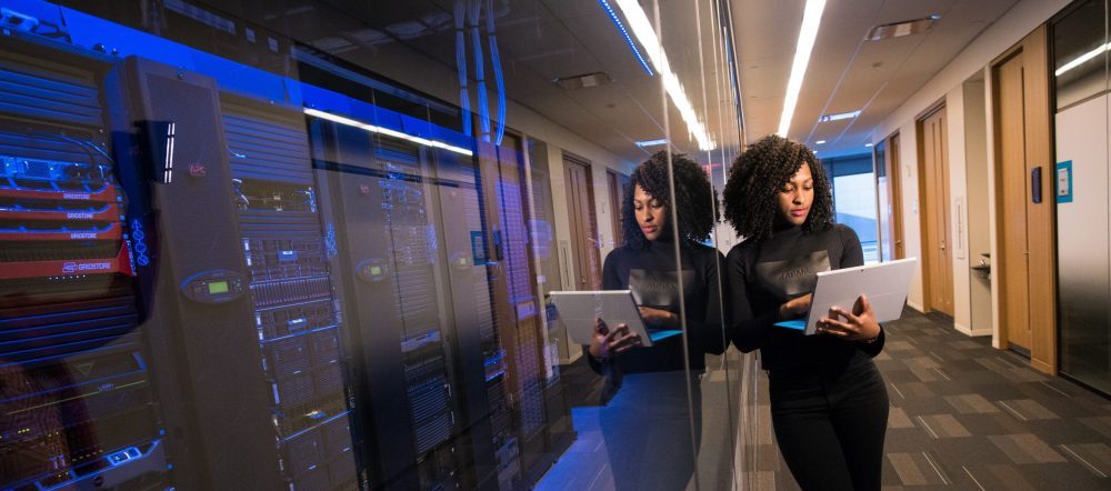 woman standing in a hallway using her laptop next to data