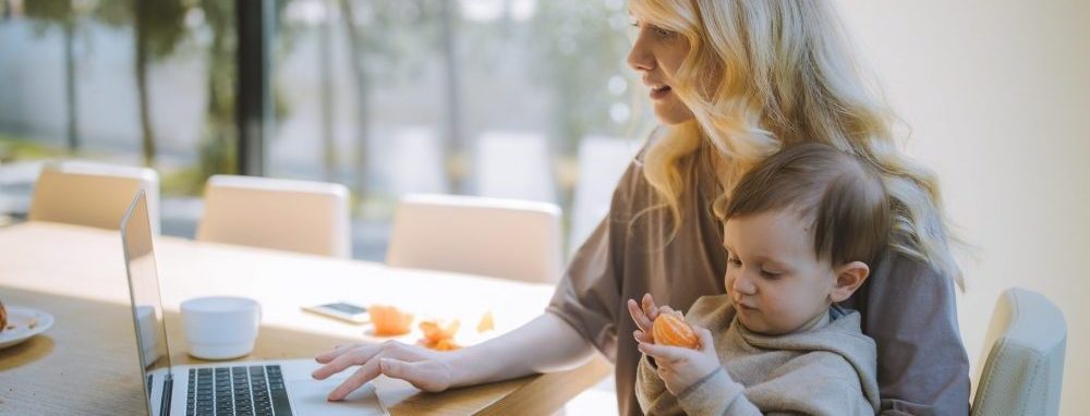 woman holding baby and working on a laptop while sitting at a table