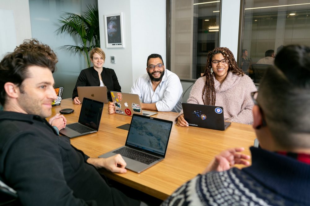 team of people sitting around a table with laptops