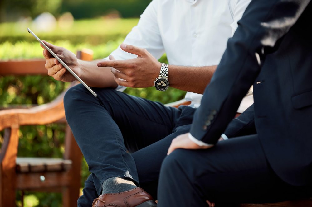 two people outside on a bench looking at a tablet