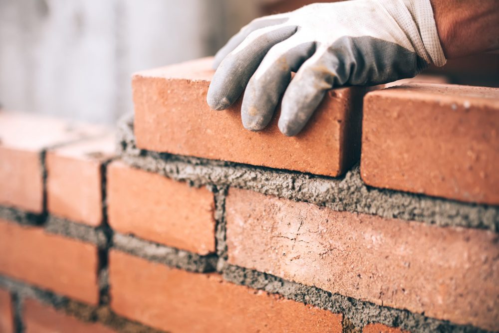 Close up of industrial bricklayer installing bricks on construct